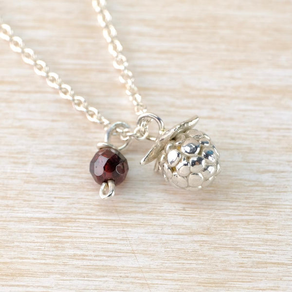 Necklace with two charms ,one blackberry, one little red garnet on a light wooden surface