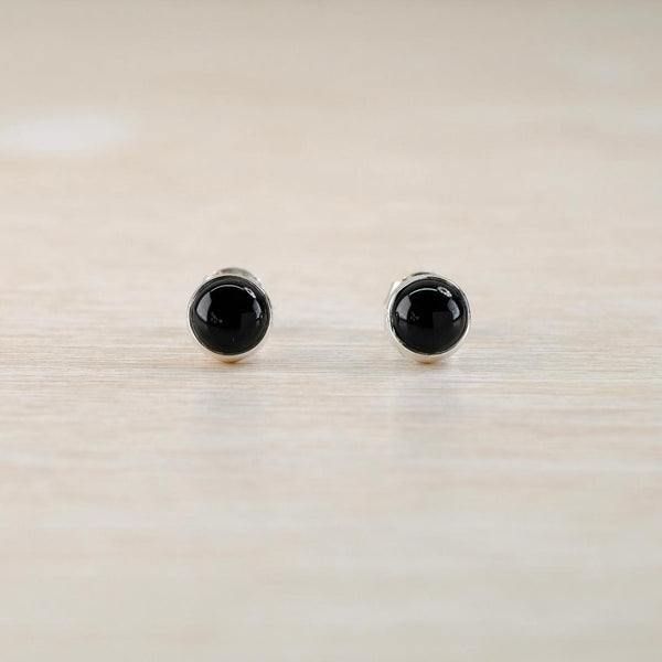 Pair of black round stud earrings on a light wood surface