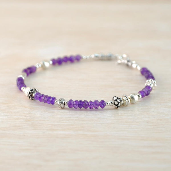 Purple beaded bracelet with silver accents on a light wooden surface