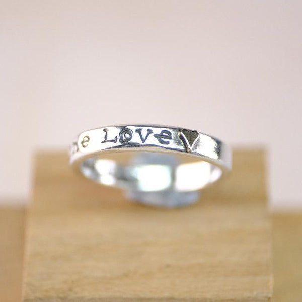 Silver ring with 'love' engraving on a wooden stand against a light background