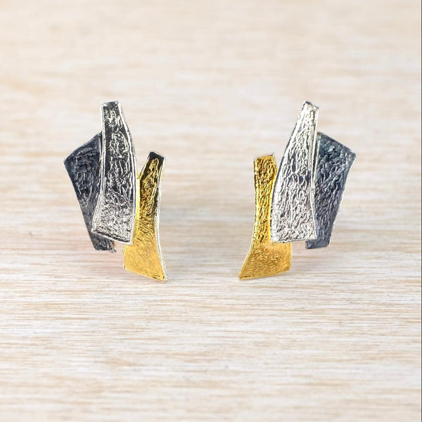 Pair of gold and silver geometric earrings on a textured beige background
