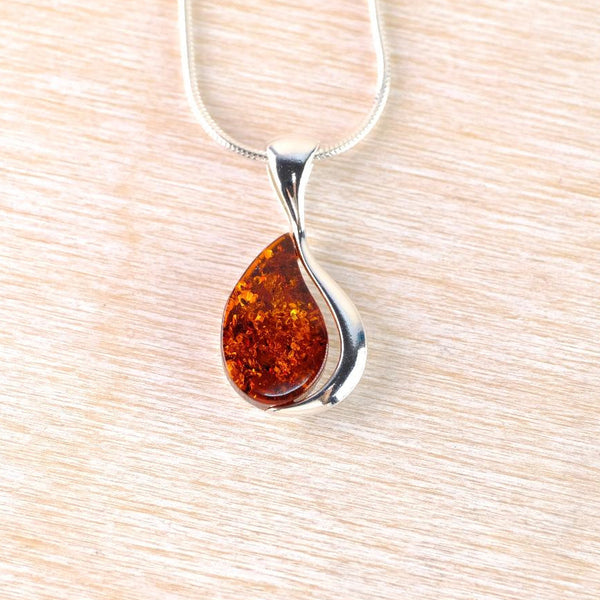 Teardrop-shaped amber pendant on a silver chain against a light wood background
