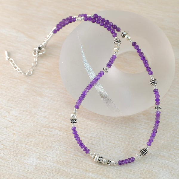Purple beaded necklace with silver accents on a light wooden surface