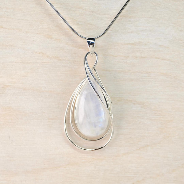 Silver pendant with a teardrop-shaped white stone on a light wood background