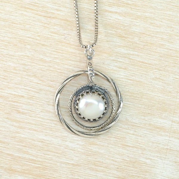 Silver necklace with a circular twisted silver spiral pendant featuring a pearl on a beige background