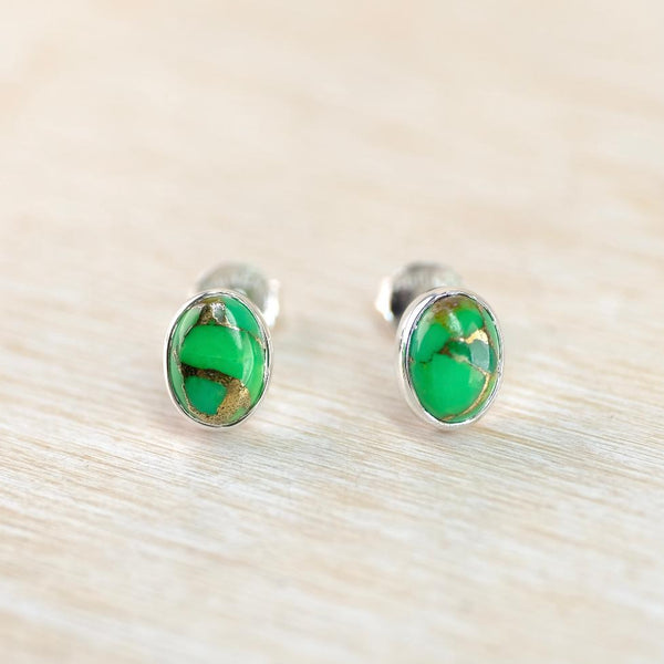 Pair of silver earrings with green gemstones on a light wooden surface