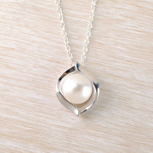 Silver necklace with a pearl pendant on a light wood surface