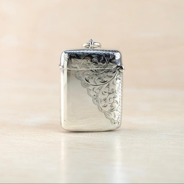 Silver decorative vesta case with intricate patterns on a beige background 