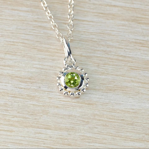 round silver pendant with green gemstone at centre, on a silver chain