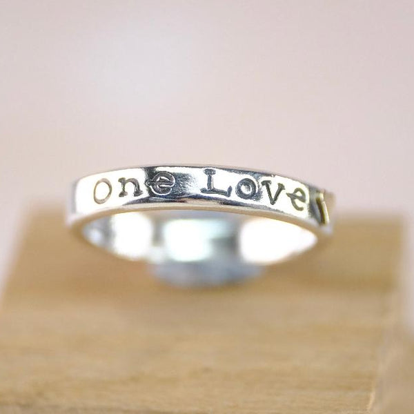 Silver ring with 'One Love' engraving and a gold heart.