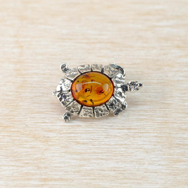 Silver turtle shaped brooch with a central amber stone on a beige textured background