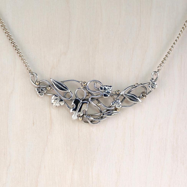Silver necklace with leaf and vine design on a light wooden background