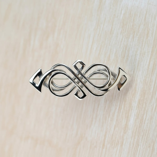 Silver infinity symbol brooch on a light wood background