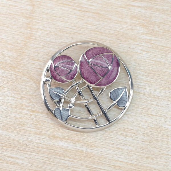 Silver brooch with purple floral design on a wooden surface