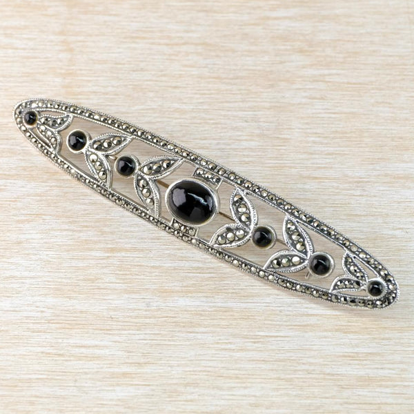 Decorative metal brooch with black gemstones on a beige textured background