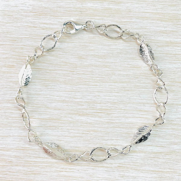 Silver linked bracelet with a textured finish. The pattern of links  is twisted oval, larger oval, twisted oval, 3D leaf design- repeated 5 times .