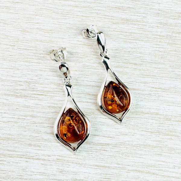 the overall shape of these earrings is an elongated tear drop. Inside an open silver tear  drop is a tear drop shaped piece of amber that fits into the silver in the middle but leaves the top and bottom open, The amber is deep browny orange with lots on interesting markings. The tear drop hangs from a silver bar attached to the post and butterfly.