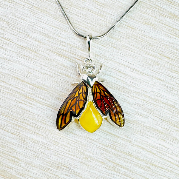 Gorgeous bee! The body is formed from an opaque yellow amber. Two wings, semi folded in, have more orange coloured clear amber set in sections to look really life like. The top of the bee's body, head, pincers and front legs are polished silver. Hanging off a plain long bale and a silver chain.