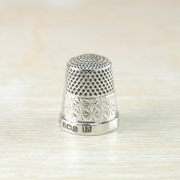 Shiny silver thimble decorated in two ways. The top half has a repeated dot indentation all over with the dots looking darker than the rest. The bottom half has delicate star shapes all round. There is a clear hallmark on the high polished rim.