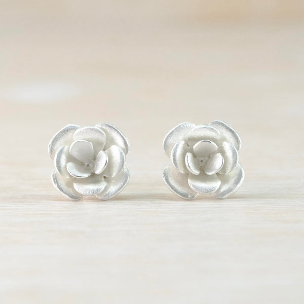 Satin silver flower earrings designed like a rose. There are 3 layers of rounded petals . Four on the outside then another four slightly smaller then three smaller in the middle.