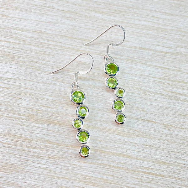  five round pale green cut stones, set in silver are joined together in a staggered line vertically. Larger stone at the top, smaller at the bottom with two medium and a small alternating between. Attached to a silver hook.