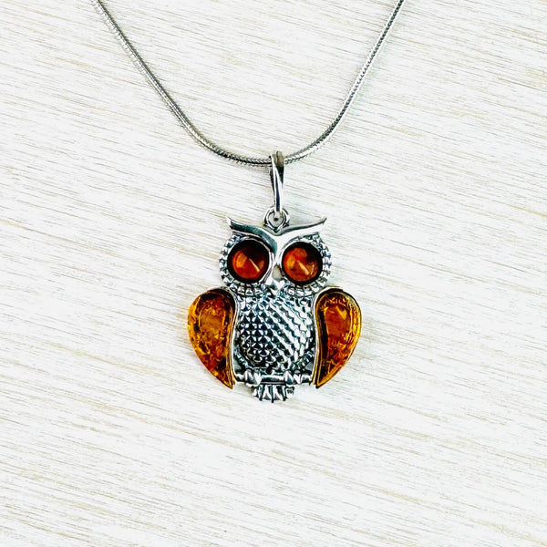 A cute owl, slightly round and fat looking! His round eyes and wings are formed from clear orange amber. His round tummy and the edges of hie eyes are in patterned silver. His feet curve around a plain silver stick, his tail shows behind this. Two polished silver shapes form his 'ears' . He hangs off a silver chain with a plain silve bail.