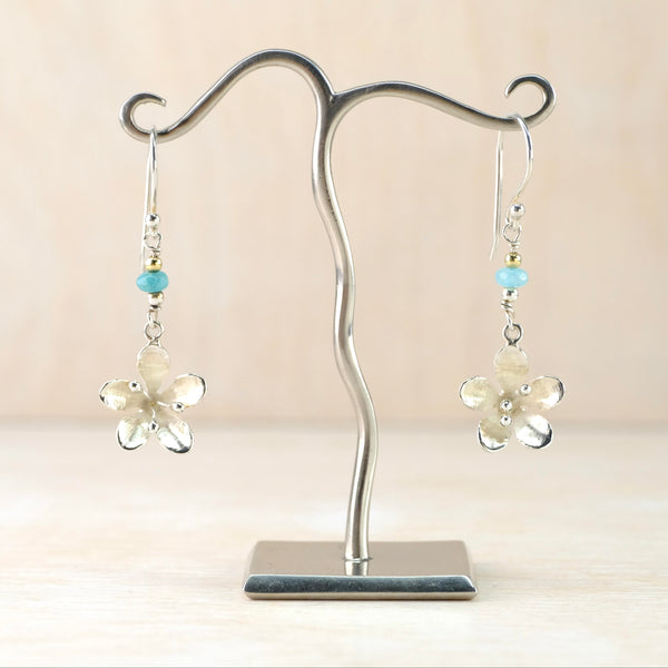 Five petalled flower in a satin silver finish has 3 stamens with silver dots in the centre, These hang below a small turquoise bead and a smaller gold plated bead which all hangs off asilver hook.