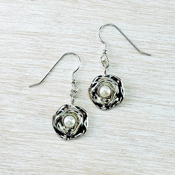 Just off round in shape, there is a small round pearl set centrally. The surround is multi layers of silver, a bit like looking into a flower. Hanging from a silver hook