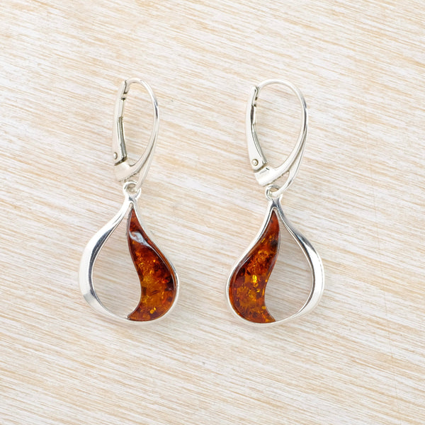 Each earring is a gentle tear drop outline. One third of the tear drop is filled with orange/ brown amber, with a curved shape. The amber has flecks of lighter and darker colours in it