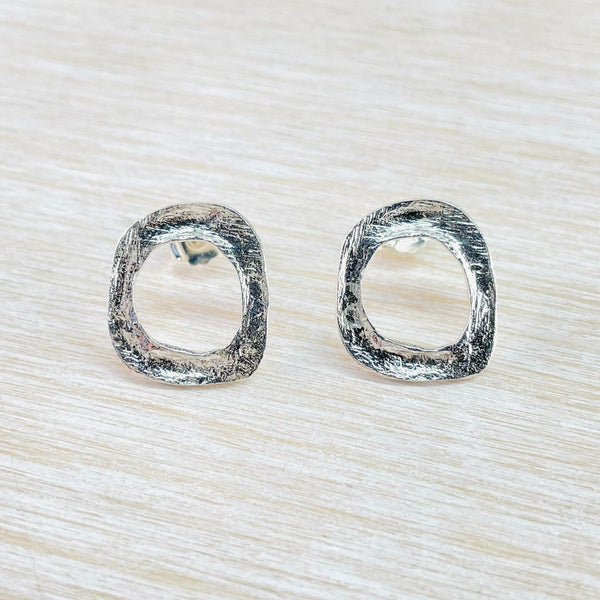 These earrings have a rounded square shape, cut out in the centre to create another rounded square shape. The silver is textured with a gentle scratched effect.