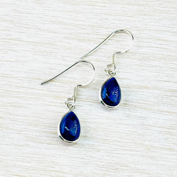 Tear drop shaped earrings hanging from a silver hook.The stone is a deep blue and simply set in a silver tear drop surround.