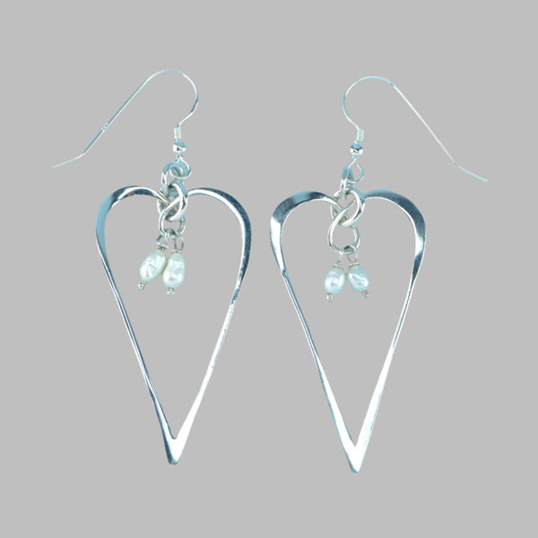 Two little irregular shaped white seed pearls hang from a silver ring at the top of an open elongated heart shape. The earrings hang from a silver hook. 