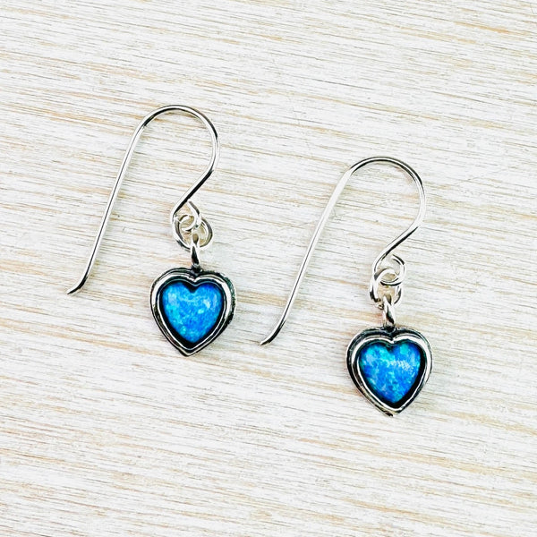 Vibrant bright blue opal stone, in a heart shape, is framed, in a heart shape, in dark silver. It hangs from a simple silver hook.