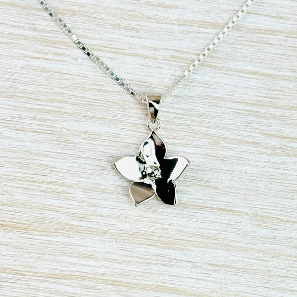 A five petalled flower, each petal is almost triangular in shape with the pointy end facing out. Very shiny and bright with a sparkly little round stone in the centre. Attached to a square chain via a plain silver bail.
