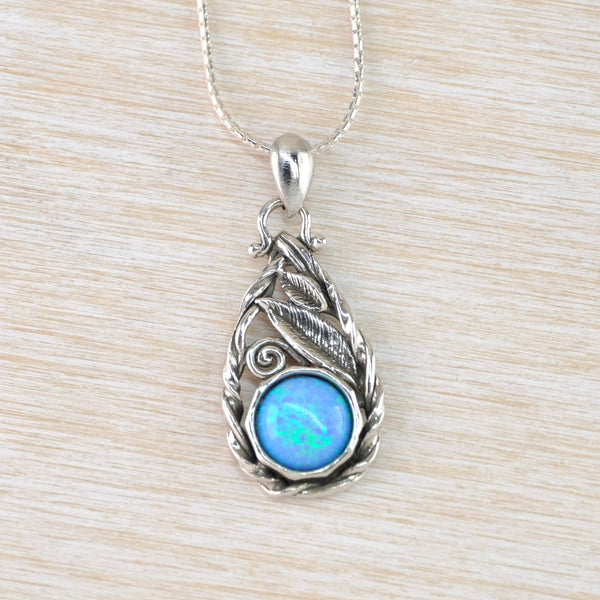 A bright blue /green round opal is set in the middle bottom of a tear drop shaped pendant. The stone is set in a shiny sillver surround, the edging of the pendant is a loose twisted oxidisd darker silver. Above the ston are two leaves and a scroll all in oxidised silver.e