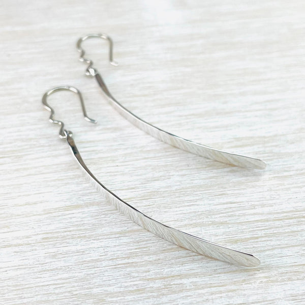 High polished plain silver earrings. Simple long shape, slightly wider at the bottom, just curves gently backwards.Hanging off a silver hook.