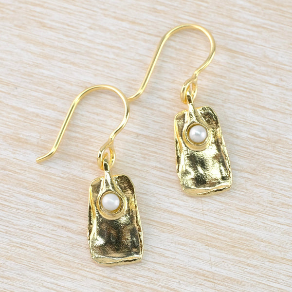 Shiny textured gold coloured off rectangular shaped drops. The top is slightly narrower than the bottom. A white pearl is nestled about a thirs of the way down.