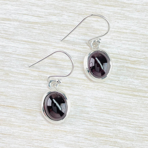 Deep dark red, smooth finish garnets are simply set in an oval shiny silver surround, Hanging from a silver hook with a silver circle to attach the hook.
