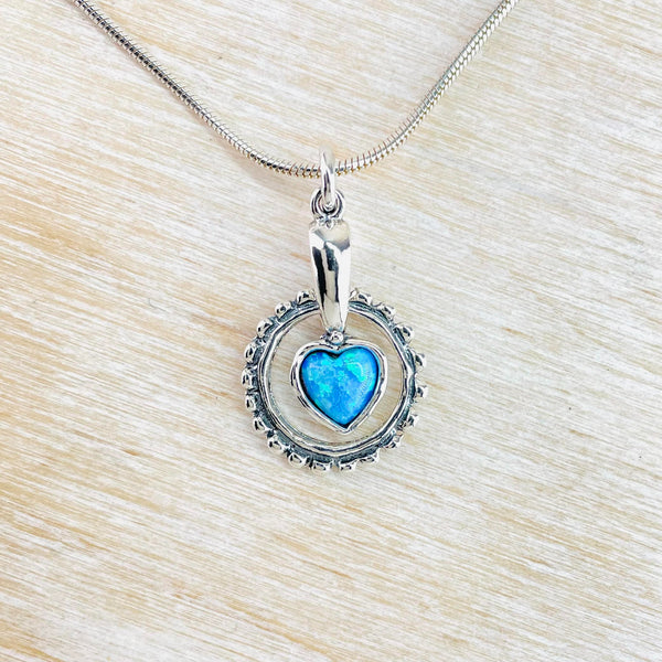 Bright blue heart shaped opal is hanging off a high polished silver stem. A decorated silver circle hangs freely through the silver stem  and around the heart - it can be spun round.