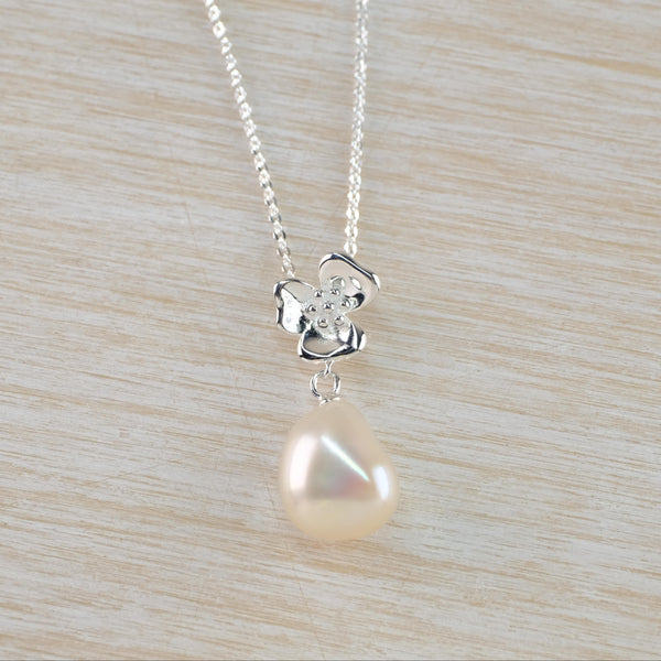 A glossy creamy tear drop pearl hangs below a three petalled flower with dots in the centre. All hang from a delicate link chain.