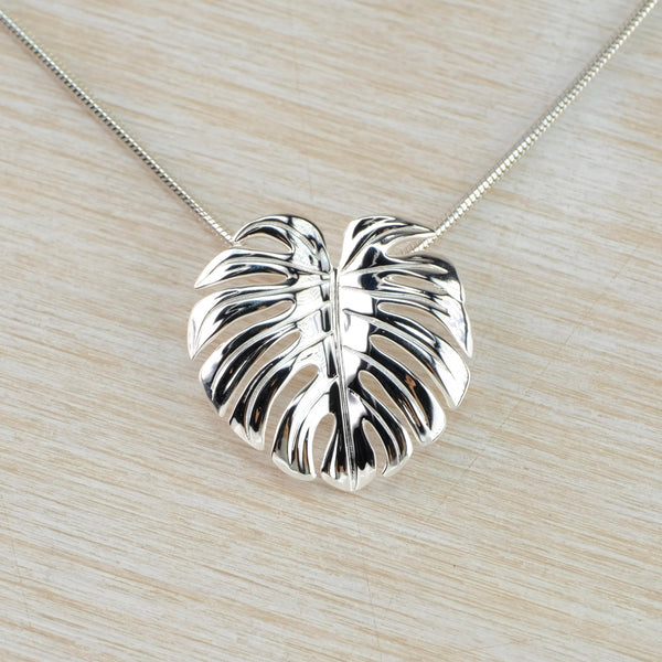 A shiny glossy looking leaf - very tropical in feel, wide with splits/holes looking like a swiss cheese. Hanging off a silver snake chain.