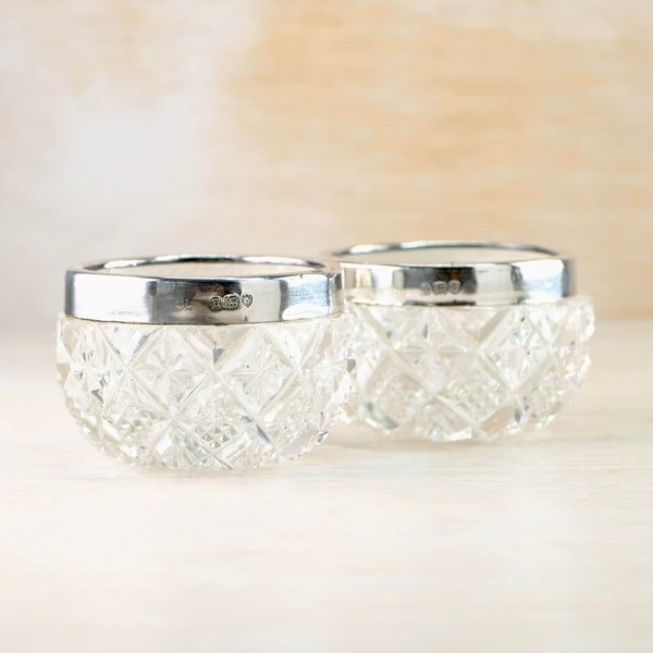 Small cut glass bowls are topped with a bright shiny silver rim, about a quarter the size of the bowl. The glass is cut with diamond shaped sections, come with star flowers cut in and others with a spotty design. Arranged in rows around the glass in alternate designs.