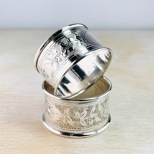 pair of round silver napkin rings with floral decoration engraved in the central sections with high polished edging.