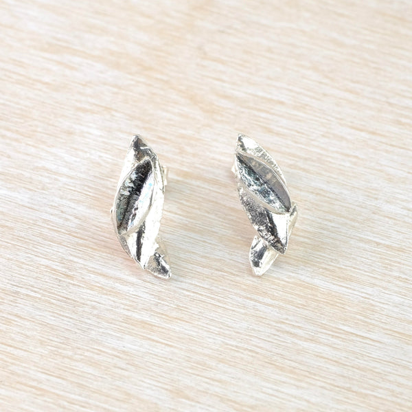The overall shape of each earring is a semi oval, mirroring each other. Each earring is made up of four little leaveslaying on top of each other, all in a textured but shiny silver.