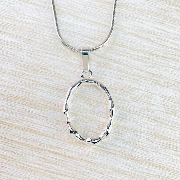 Shiny silver in an open oval shape with a regular 'lumpy' design in the silver. Simply connected to the chain by a plain silver bale.