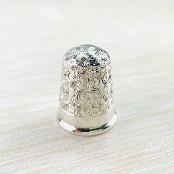 silver thimble covered in starburst shaped floral design with a plain silver band at the bottom.