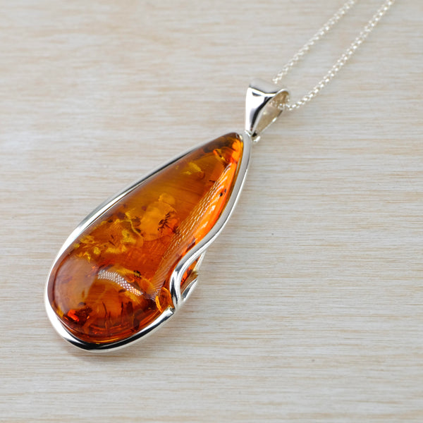 Beautful deep orange, tear drop shaped amber is framed in bright silver. on the left side the silver has a small curve to cover a little of the stone. There are small bits within the amber , the rest is clear and bright.