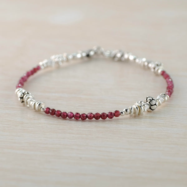 A red and silver bracelet formed of little round red garnet beads in three groups of twelve, interspersed with a collection of different silver beads in differeing sized, shapes and finishes.