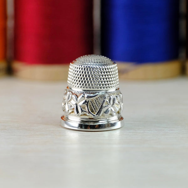 Silver thmble, the top half is decorated with repeated dimples, the bottom half has shamrock leaves  with an Irish harp in the centre front. The bottom is a high polished plain silver