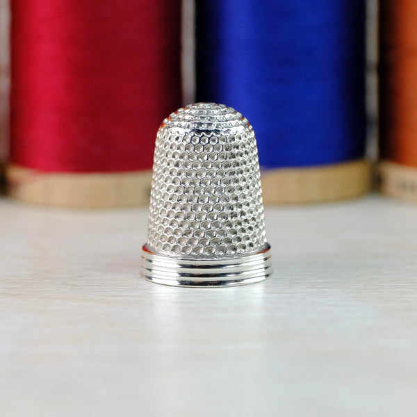 Shiny silver thimble with three shiny silver bands around the rim at the bottom and all-over dimpling on the rest.